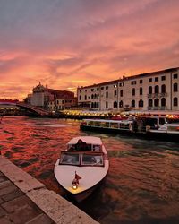 Boat in canal by buildings against sky during sunset