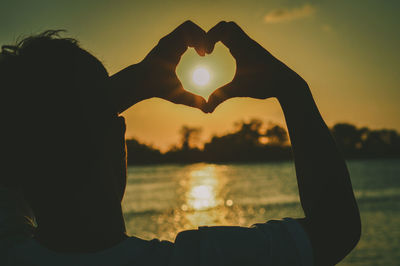 Close-up of silhouette hand holding heart shape against sky during sunset