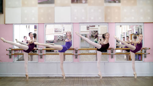 In dancing hall, young ballerinas in purple leotards perform attitude efface on pointe shoes