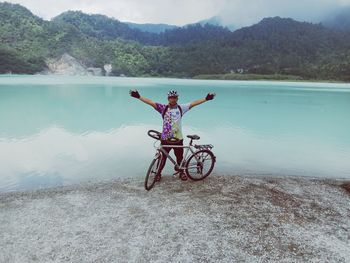 Man with arms raised on lake against mountain