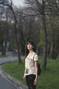 Thoughtful woman standing against bare trees at park
