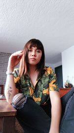 Portrait of young woman sitting against wall at home