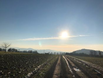 Road amidst agricultural field against sky during sunset