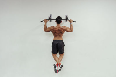 Mid adult sportsman doing chin-ups with exercise equipment on white wall