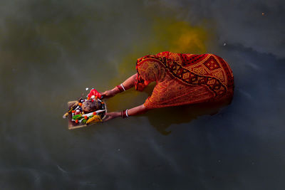 High angle view of woman holding religious offerings in lake