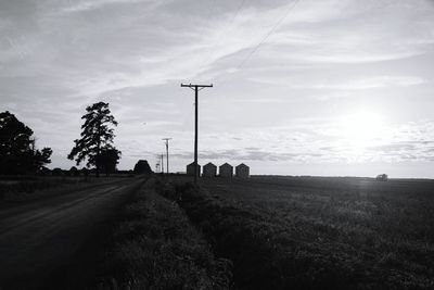 Electric poles on grassy field against sky