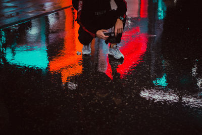 Low section of person photographing while crouching on wet street