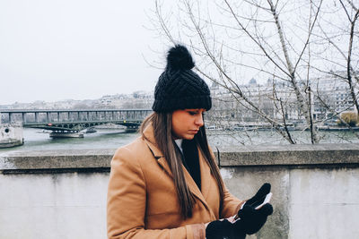 Young woman standing by river against sky in city