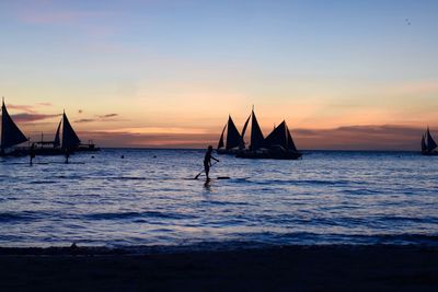 Silhouette man sailing on sea against sky during sunset