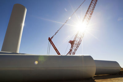 Low angle view of crane and pipes on field against sky on sunny day