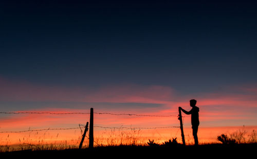 Silhouette man standing on field against sky during sunset