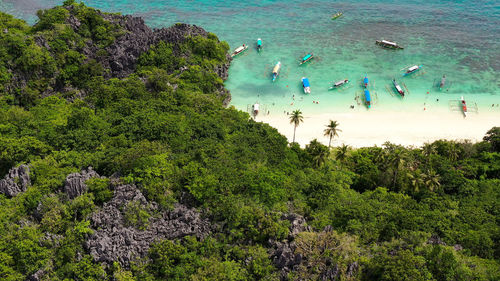 Sandy beach with tourists and tropical island by atoll. lahos island, caramoan islands, philippines.