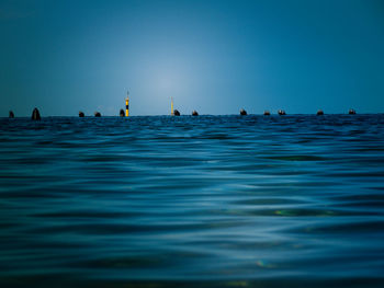 People swimming in sea against clear blue sky