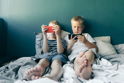 Brothers using mobile phone while sitting on bed