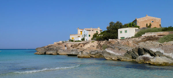 Buildings by sea against clear blue sky