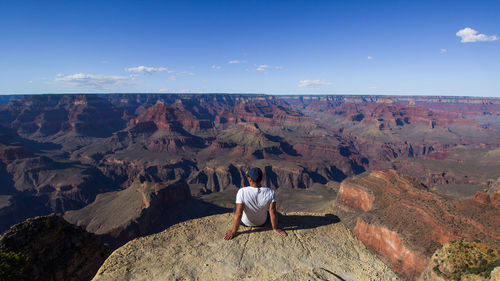 Rear view of man sitting on mountain against sky