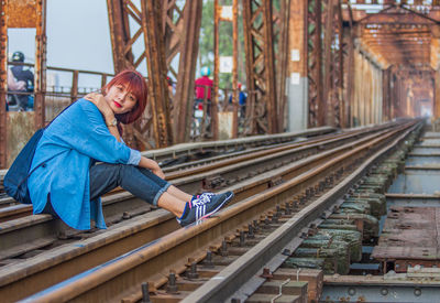 Side view of woman sitting on railroad track