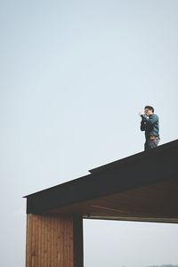 Low angle view of man photographing against clear sky