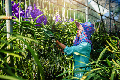 Side view of female researcher examining plants in greenhouse