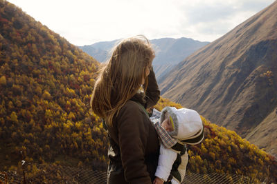 Portrait of woman with her little daughter in ergo carrier on a background of autumn mountains.