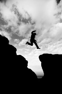 Silhouette man jumping on rock against sky