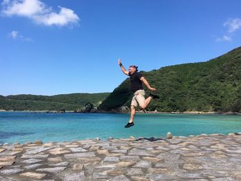 Full length of man jumping by sea against blue sky