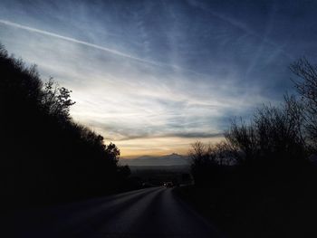 Road amidst silhouette trees against sky during sunset