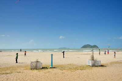 Children flying kites at beach against blue sky