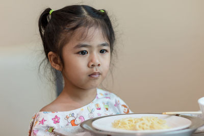 Thoughtful girl with food on table sitting against wall at home