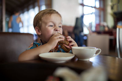Boy eating sandwich at table in cafe