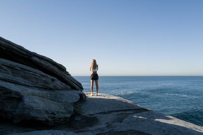 View from behind of a woman standing on the cliff overlooking the ocean