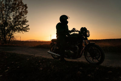 Faceless biker in helmet riding motorcycle in evening sundown on rural road