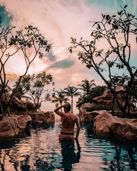 Full length of shirtless man standing in lake against trees