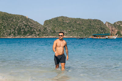 Full length of shirtless man standing on sea against sky