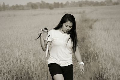 Young woman holding camera while walking on grassy field