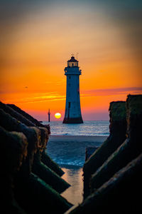 Lighthouse by sea against sky during sunset