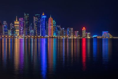 Illuminated buildings by sea against sky at night