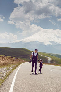 Father teaches son to ride a black skateboard on the road against of mount everest in the summer