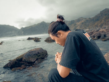 Woman sitting on rock at beach against sky