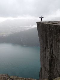 Distant view of man standing at preikestolen against cloudy sky