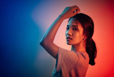 Side view portrait of young woman standing against colored background