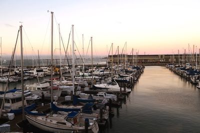 Boats moored in harbor at sunset