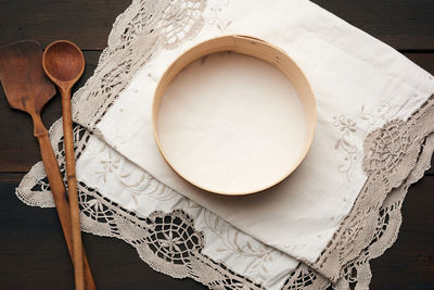 Wooden spoon and round sieve lie on a white napkin, wooden table, top view