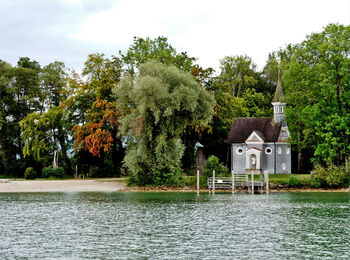 House by lake and trees against sky