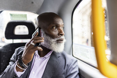 Senior businessman talking on smart phone and looking through window in taxi