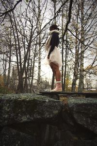 Side view of woman standing by tree in forest