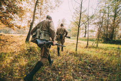 Rear view of army soldiers with guns walking in forest