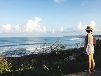 Rear view of woman standing on beach against sky