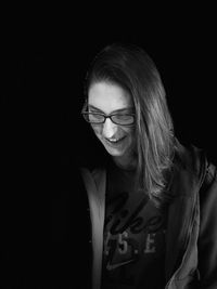 Smiling young woman wearing jacket and eyeglasses standing against black background