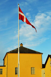 Low angle view of danish flag waving against yellow building